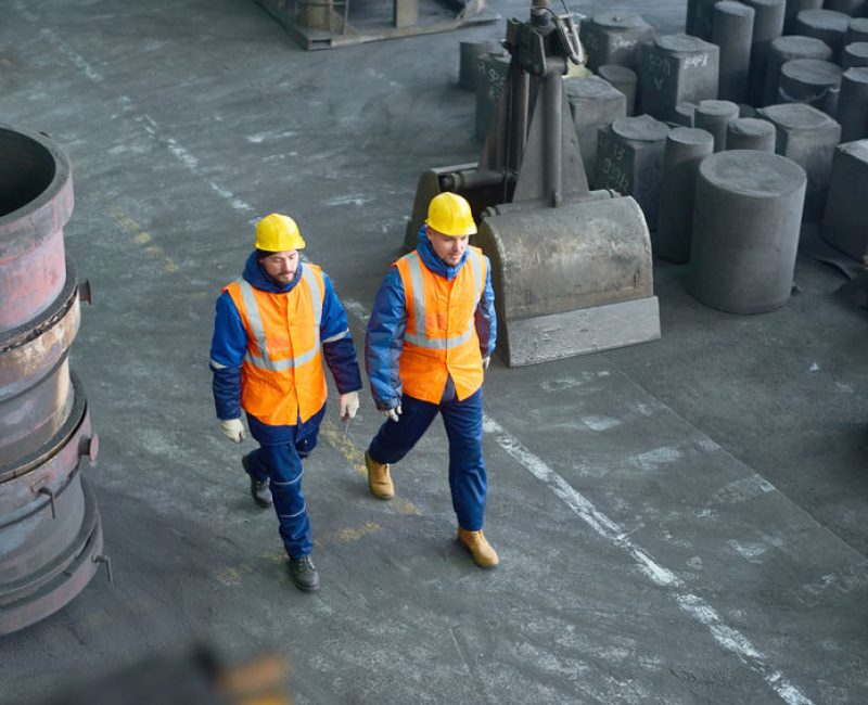 High angle view of two bearded technicians wearing uniform and hardhats walking along production department of modern plant