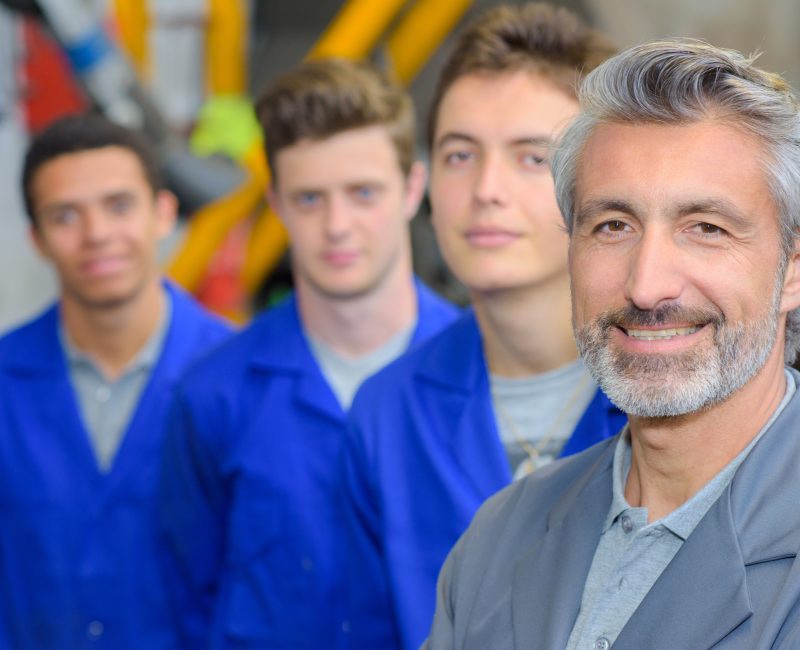 Portrait of teacher stood in front of his three apprentices